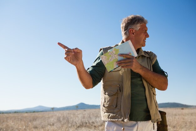 風景の上に立っている間指す地図を持つ男
