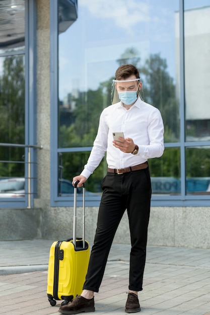Man with mask and luggage checking mobile