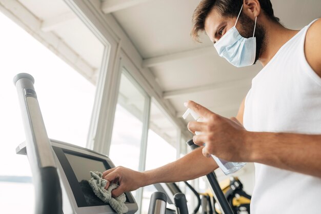 Man with medical mask disinfecting gym equipment