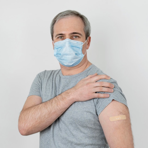 Man with medical mask showing bandage on arm after vaccination