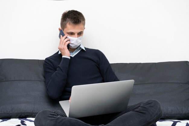 Man with medical mask using laptop and smartphone
