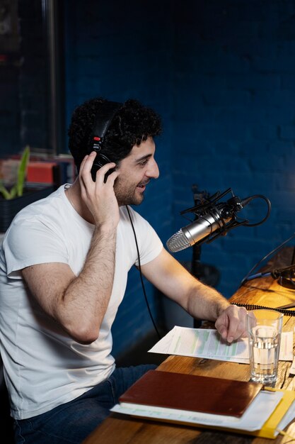 Мужчина с микрофоном и наушниками ведет подкаст в студии