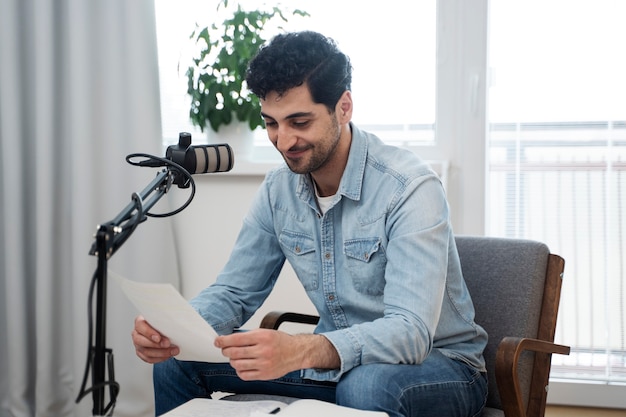 Мужчина с микрофоном ведет подкаст в студии и читает газеты