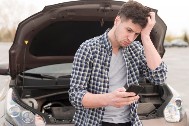 壊れた車の横にある携帯電話を持つ男