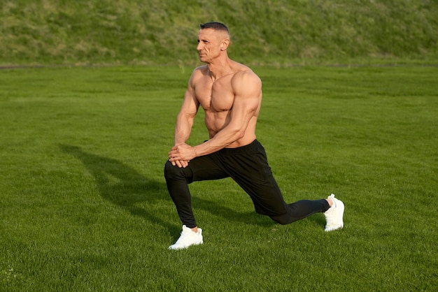 Free photo man with muscular bare torso stretching legs outdoors