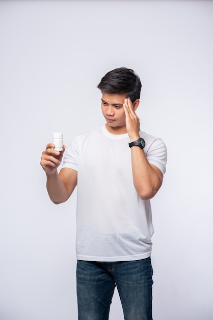 A man with pain in her hand holds a medicine bottle and the other hand but on him head