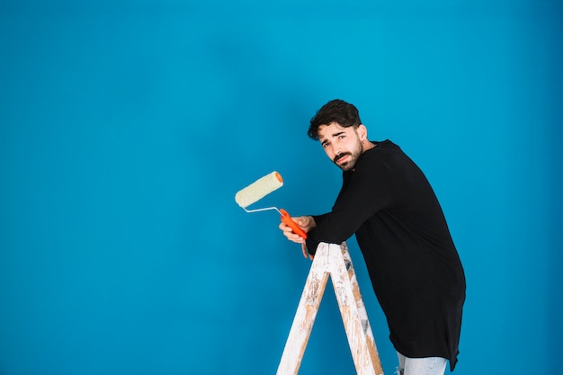 Free photo man with paint roll on ladder