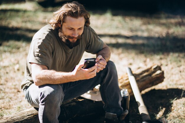 Man with phone by bonfire in forest