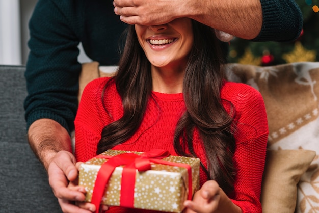 Man with present closing eyes to happy woman