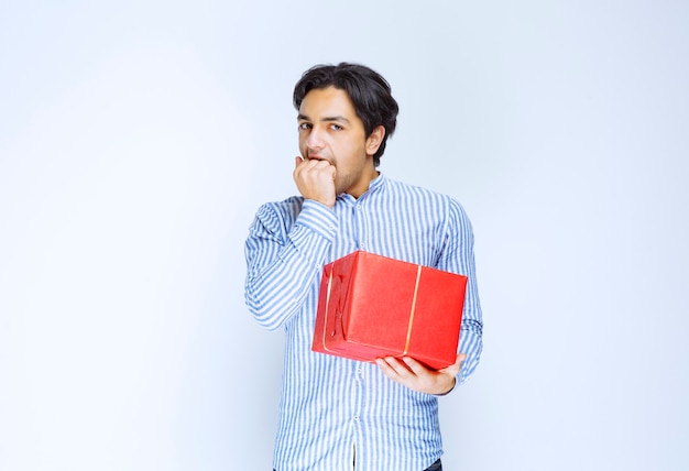 Man with a red gift box looks scared and terrified. High quality photo