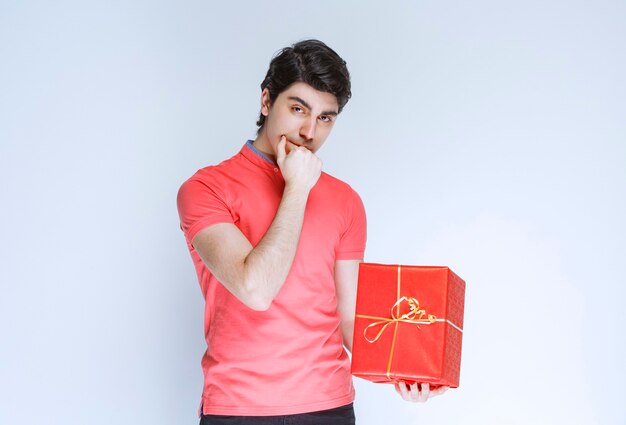 빨간색 선물 상자가 그의 입에 손을 넣고 생각하는 남자.