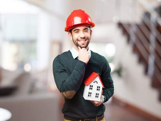 Man with red helmet and a small house in hand