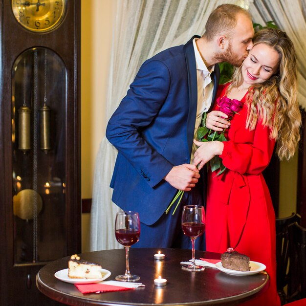Мужчина с розами целует красотку в щеку в ресторане
