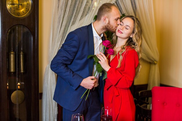 Man with roses kissing woman on cheek in restaurant