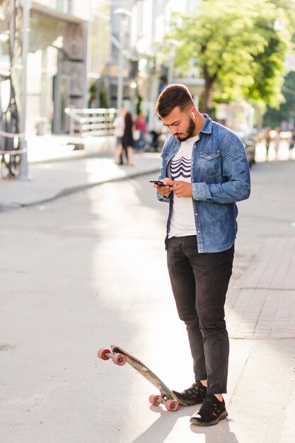 Человек с скейтбордом с помощью мобильного телефона