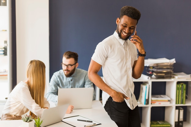 Man with smartphone leaning on table near colleagues