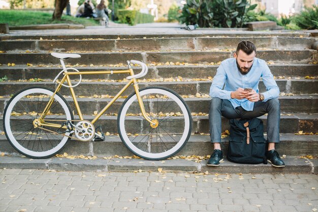 自転車の近くに座っているスマートフォンを持つ男