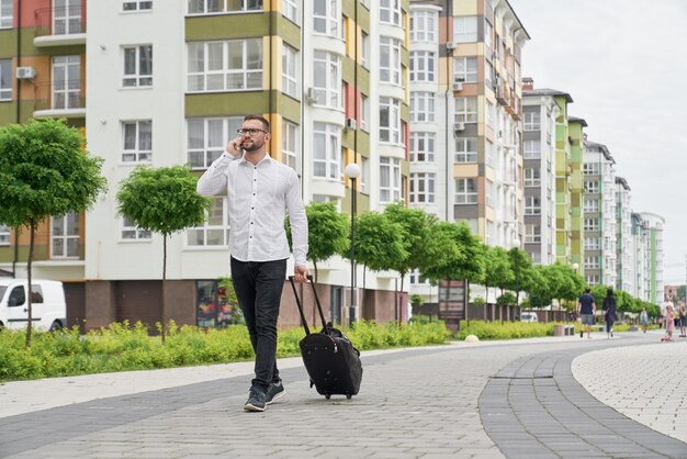 電話で話している通りを歩いてスーツケースを持つ男