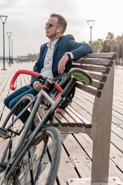 彼の自転車の隣のベンチに座っているサングラスをかけた男