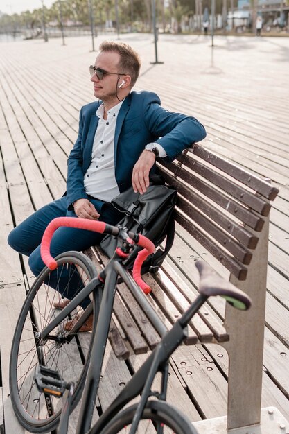 Человек в темных очках сидит на скамейке рядом со своим велосипедом