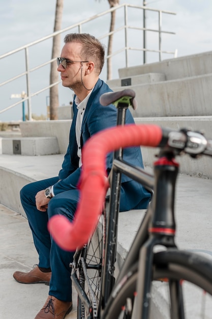 屋外で自転車の横に座っているサングラスをかけた男