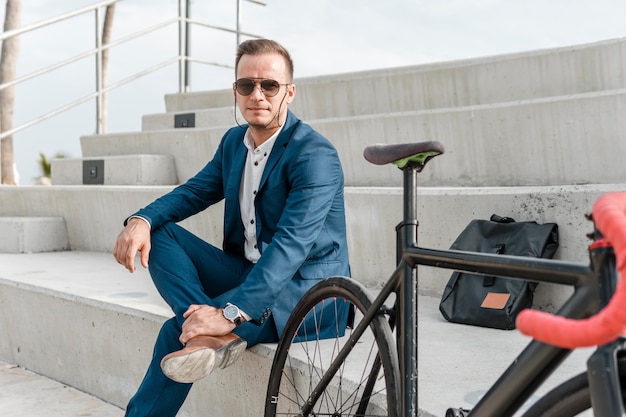 屋外で自転車の横に座っているサングラスをかけた男