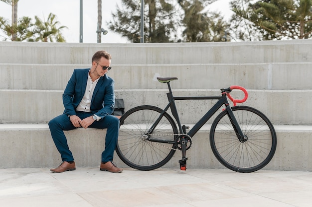 Foto gratuita uomo con occhiali da sole seduto accanto alla sua bici fuori