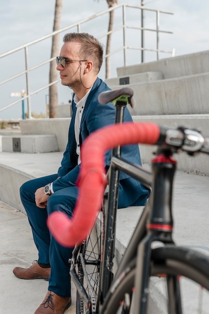 Человек в темных очках сидит рядом со своим велосипедом на открытом воздухе