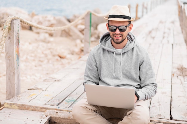 Foto gratuita uomo con gli occhiali da sole che lavora al computer portatile alla spiaggia