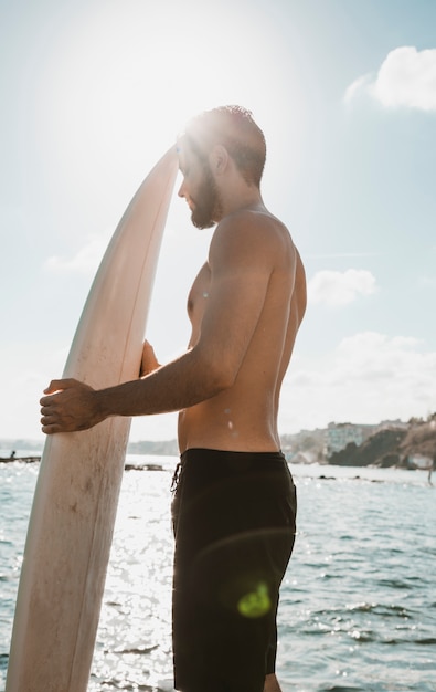 Uomo con tavola da surf in piedi contro il cielo luminoso