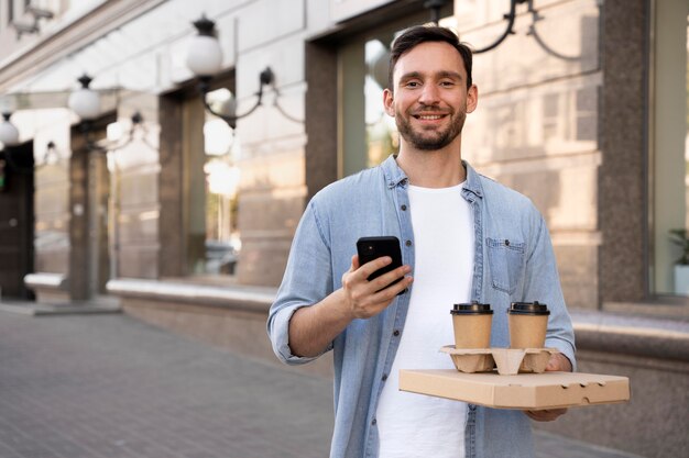 スマートフォンを使用して路上で持ち帰り用の食べ物を持つ男