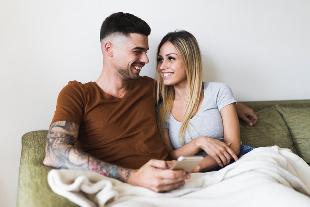 Man with tattoo over hand holding cell phone looking at her girlfriend