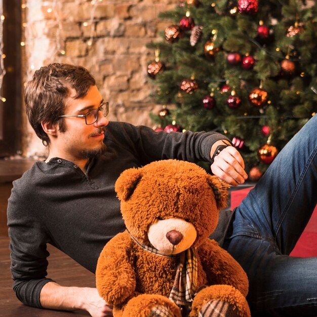 Man with teddy on floor in front of christmas tree