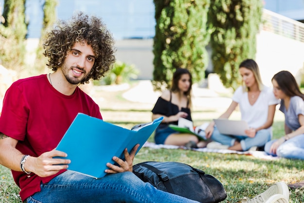 Uomo con il libro di testo che si siede sulla terra vicino agli amici