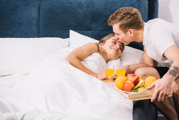 Man with tray of food kissing sleeping woman on forehead