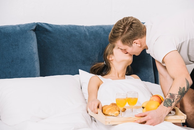 Man with tray of food kissing woman in bed 