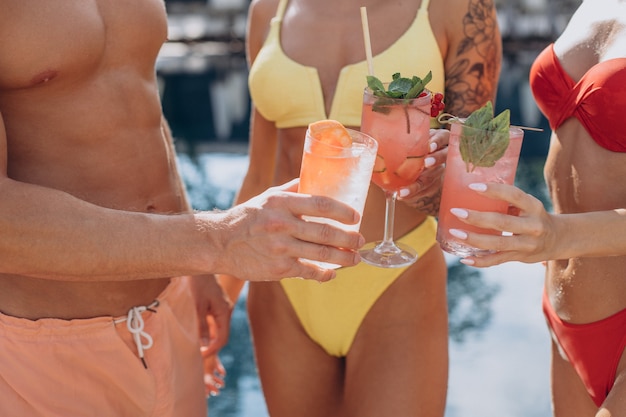 Man with two women by the pool drinking cocktails and having fun by the pool