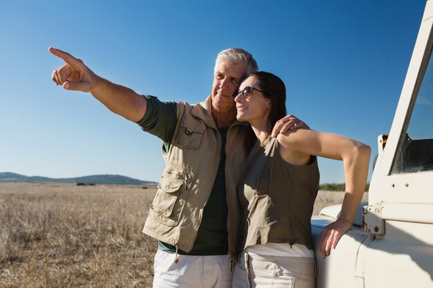 Man with woman pointing by vehicle on field