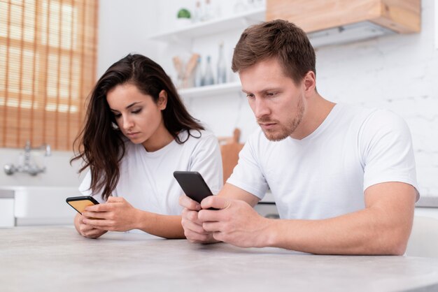 Мужчина и женщина проверяют свои телефоны на кухне