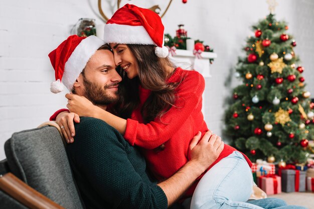 Man and woman in Christmas hats embracing on sofa