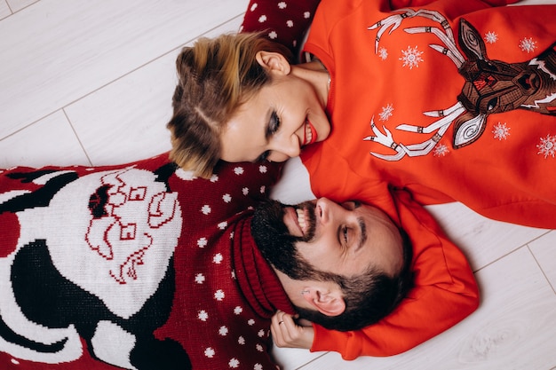 Man and woman in Christmas sweaters hug each other tender lying