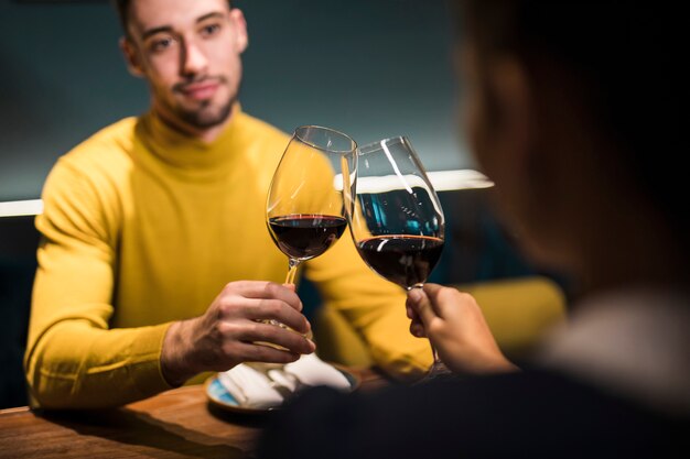 Man and woman clanging glasses of wine and sitting at table