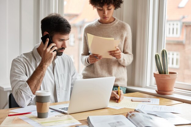 Man and woman colleagues makes research for startup project, pose near desktop.