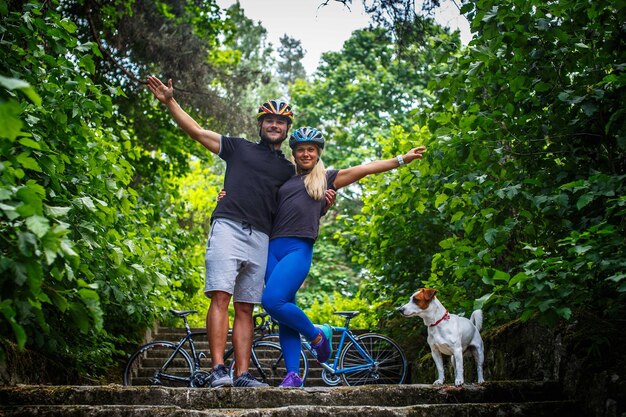 Man and woman in cyclist helmets posing on steps with sport bicycles on background.