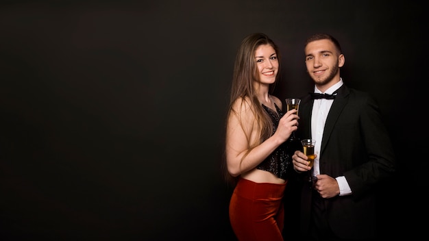 Man and woman in dinner jacket and evening wear with glasses of drinks 