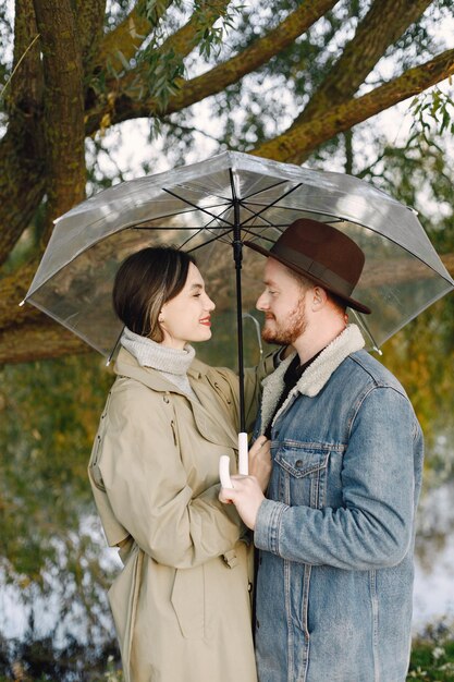 Мужчина и женщина в модной одежде отдыхают на природе у озера вместе под прозрачным зонтиком