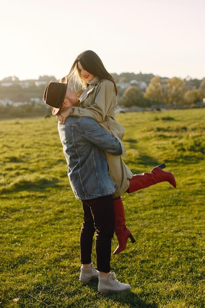 Man and woman in fashion clothes resting on a nature together. Man wearing jacket and a black hat and woman skirt and red boots