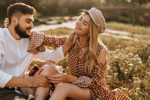 Man and woman gently stroke each other while sitting on grass. Romantic couple smiling poses with labrador.