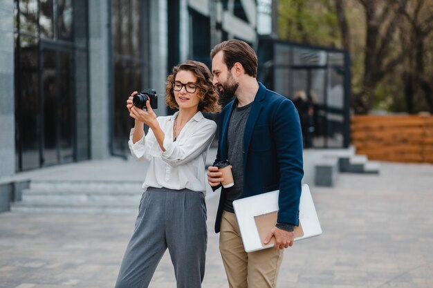 Man and woman going on stairs in urban city center, holding coffee and laptop, discussing