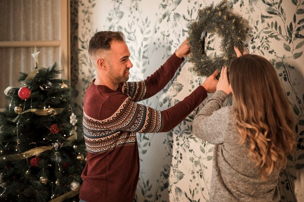 男性と女性は、装飾されたモミの木の近くにクリスマスの花輪をぶら下げ